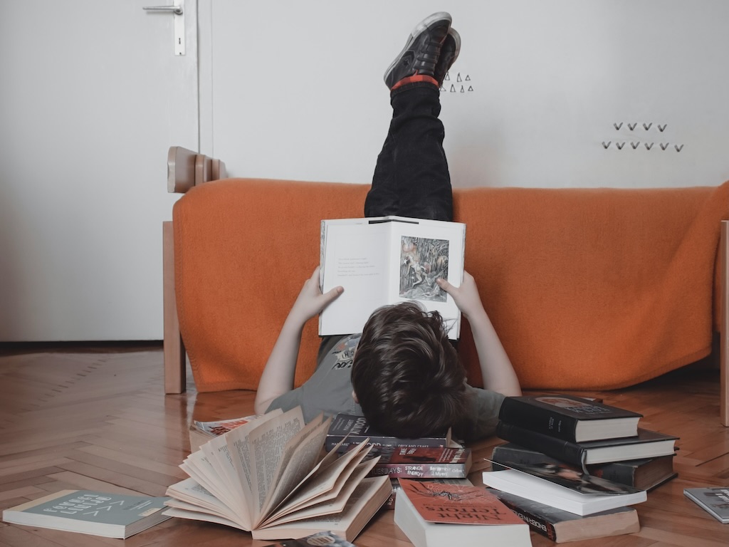 een jongen leest een boek en ligt omring door boeken op de grond